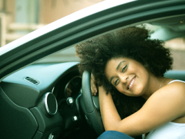 Mulher dirigindo um carro sorrindo com o vidro aberto.